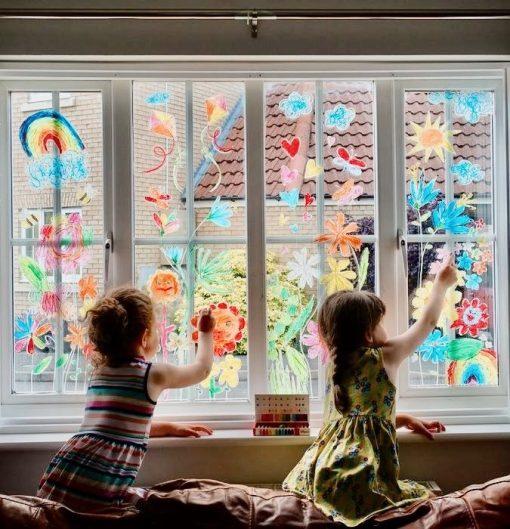 Kinder zeichnen mit Fensterkreide auf Fenster